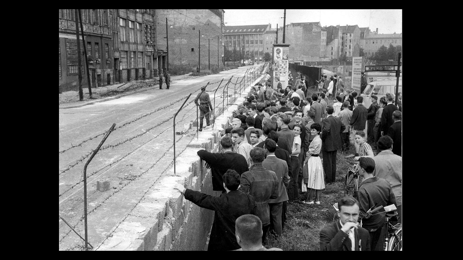 Impresionante contraste entre los dos sectores de Berlín, el 30 de agosto de 1961: a la derecha un grupo muy numeroso de berlineses occidentales contemplan con curiosidad el aspecto desolado de una de las calles de Berlín Oriental, sólo ocupada por miembros de la llamada «Policía Popular» 